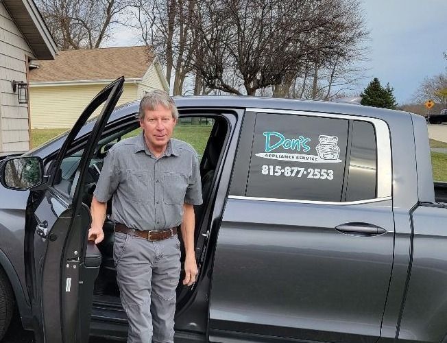 Man exiting a gray pickup truck with business logo on the window. He wears a gray shirt and pants.