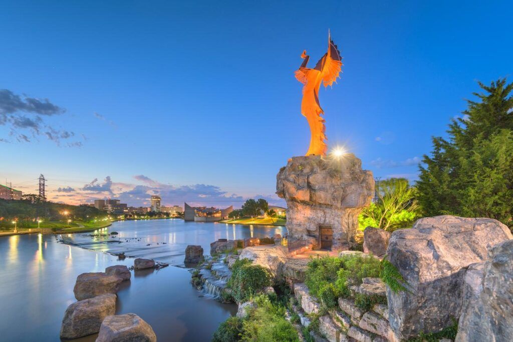 A statue standing on a rocky base near a body of water during twilight.
