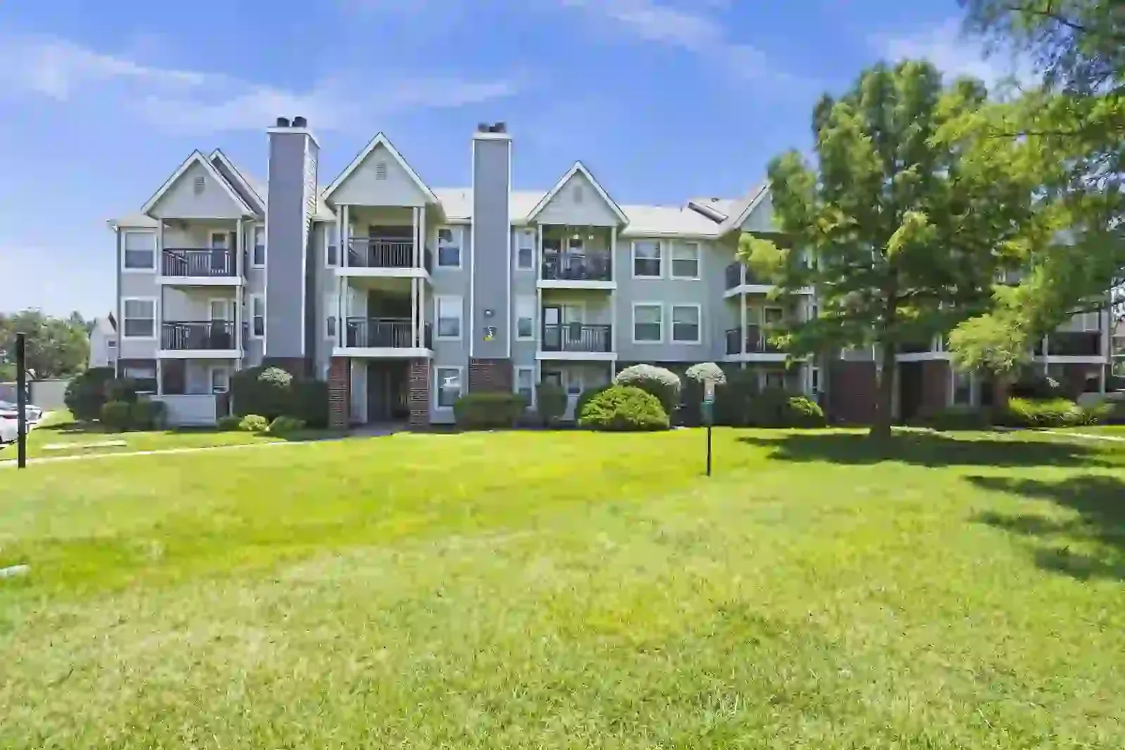 Image of a multi-story apartment building with green grass and trees in the foreground.