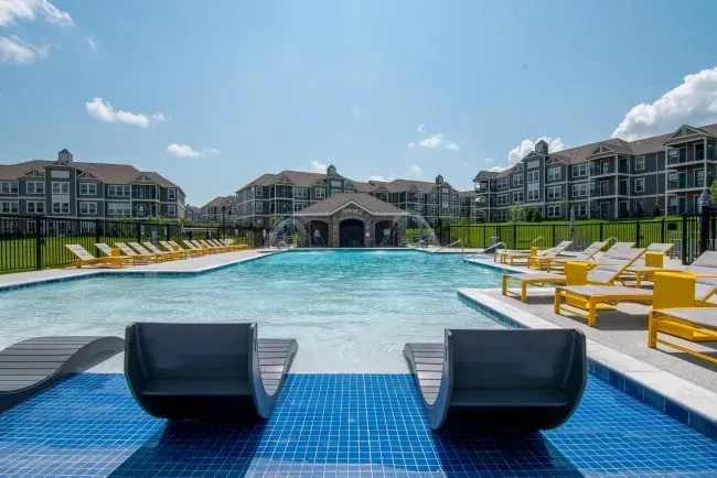 View of a swimming pool with lounge chairs and surrounding apartments.
