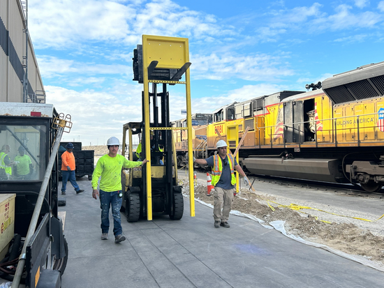 Workers removing roof debris, with one shoveling into a black bag, and another sweeping. Other workers are also present on the roof.