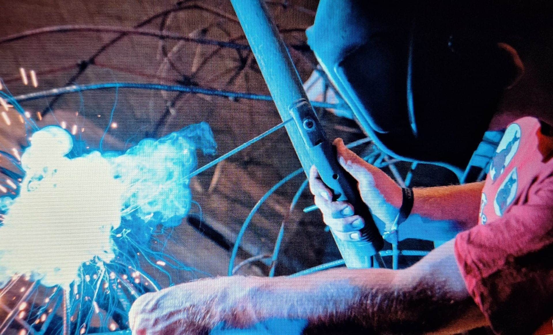 Een arbeider gebruikt een lasbrander; felblauwe vonken verlichten een donkere industriƫle omgeving.
