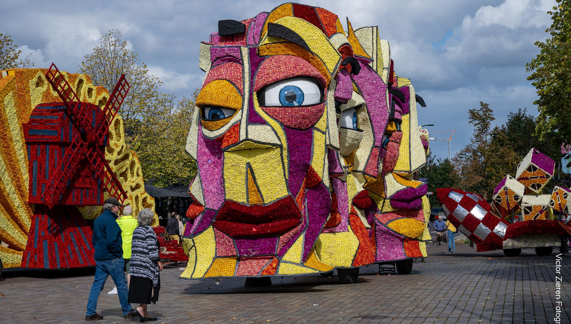 Mensen staan ​​naast een kleurrijk mozaïekgezicht dat buiten onder een bewolkte hemel tentoongesteld wordt.