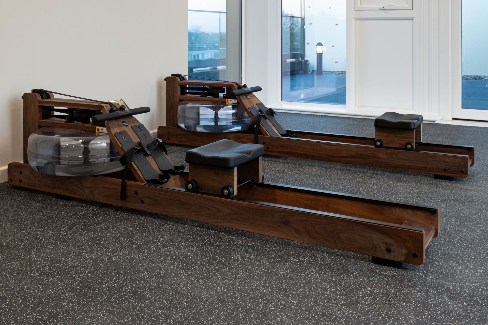 Two wooden rowing machines are sitting on a rubber floor in a gym at Walton Court.