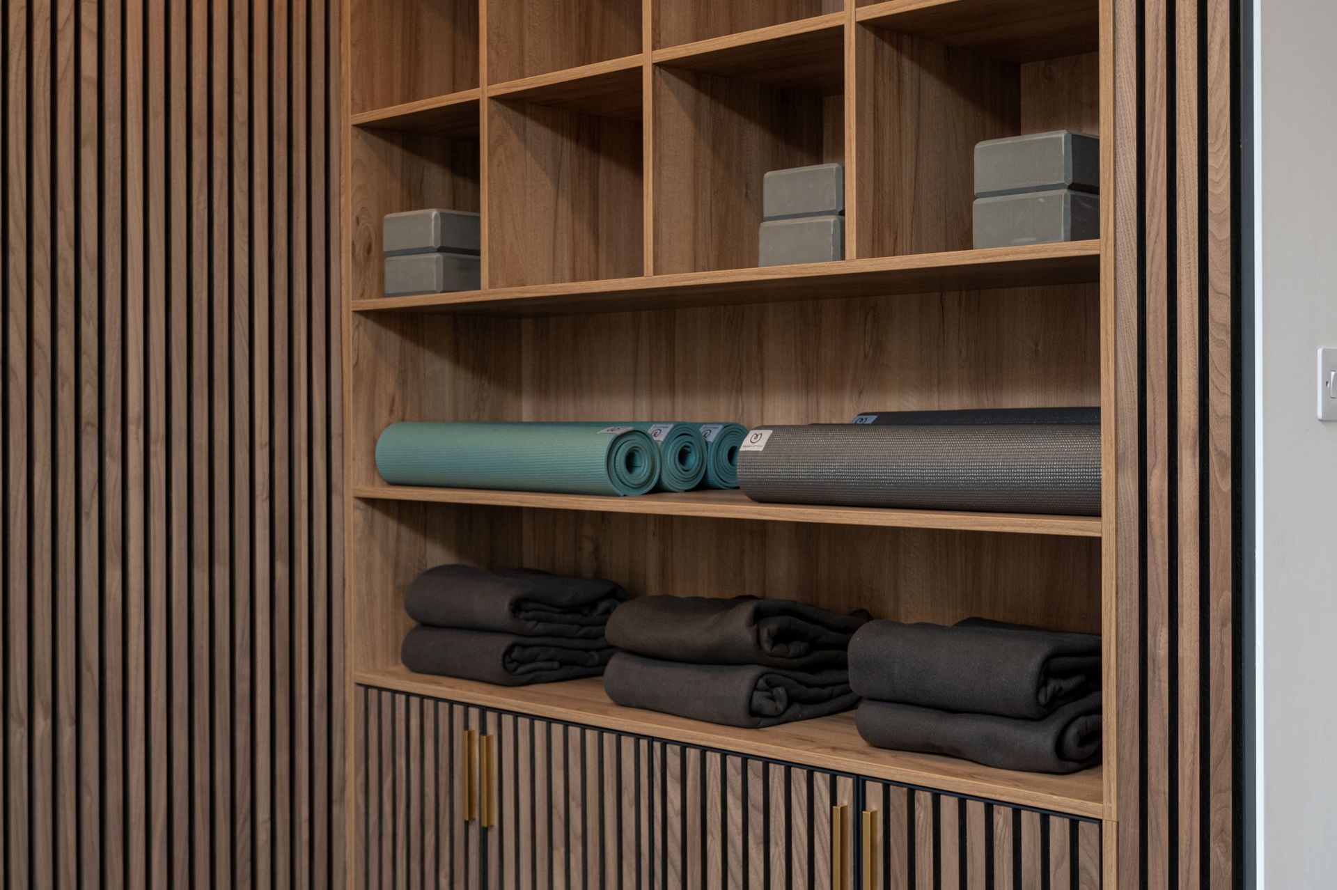 A wooden shelf filled with yoga mats and towels at Walton Court.