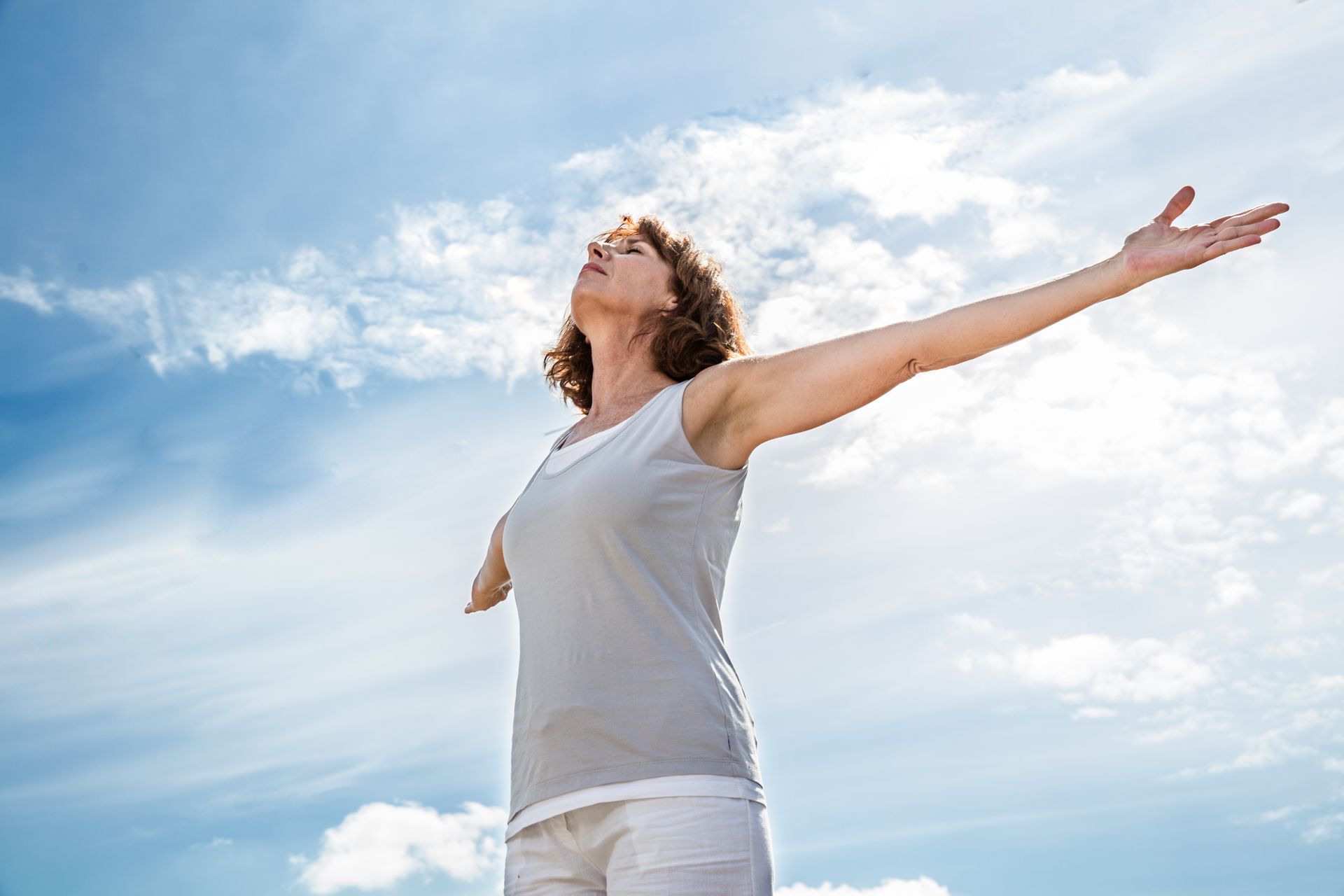 A woman is standing with her arms outstretched in front of a blue sky.
