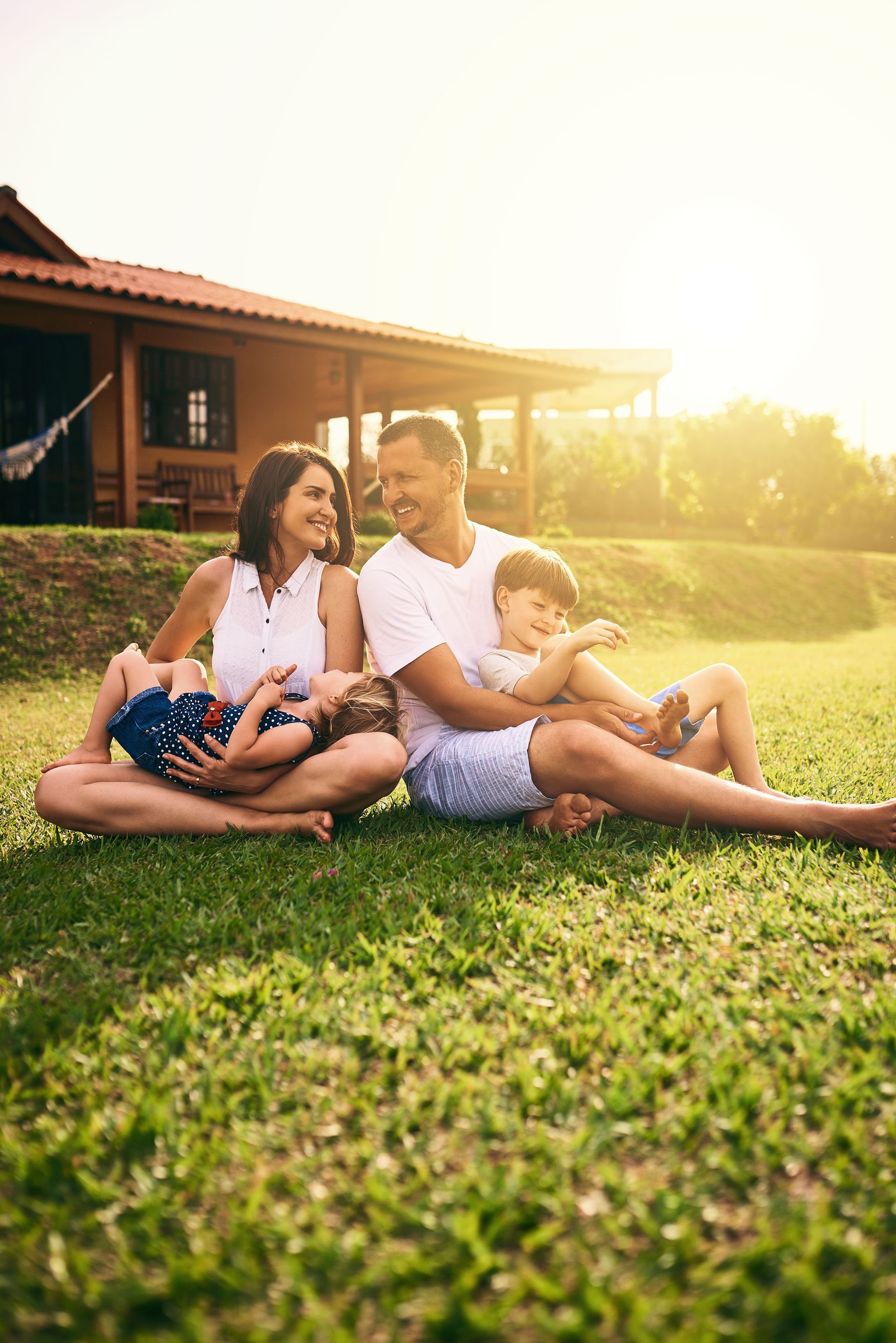 A family is sitting on the grass in front of a house.