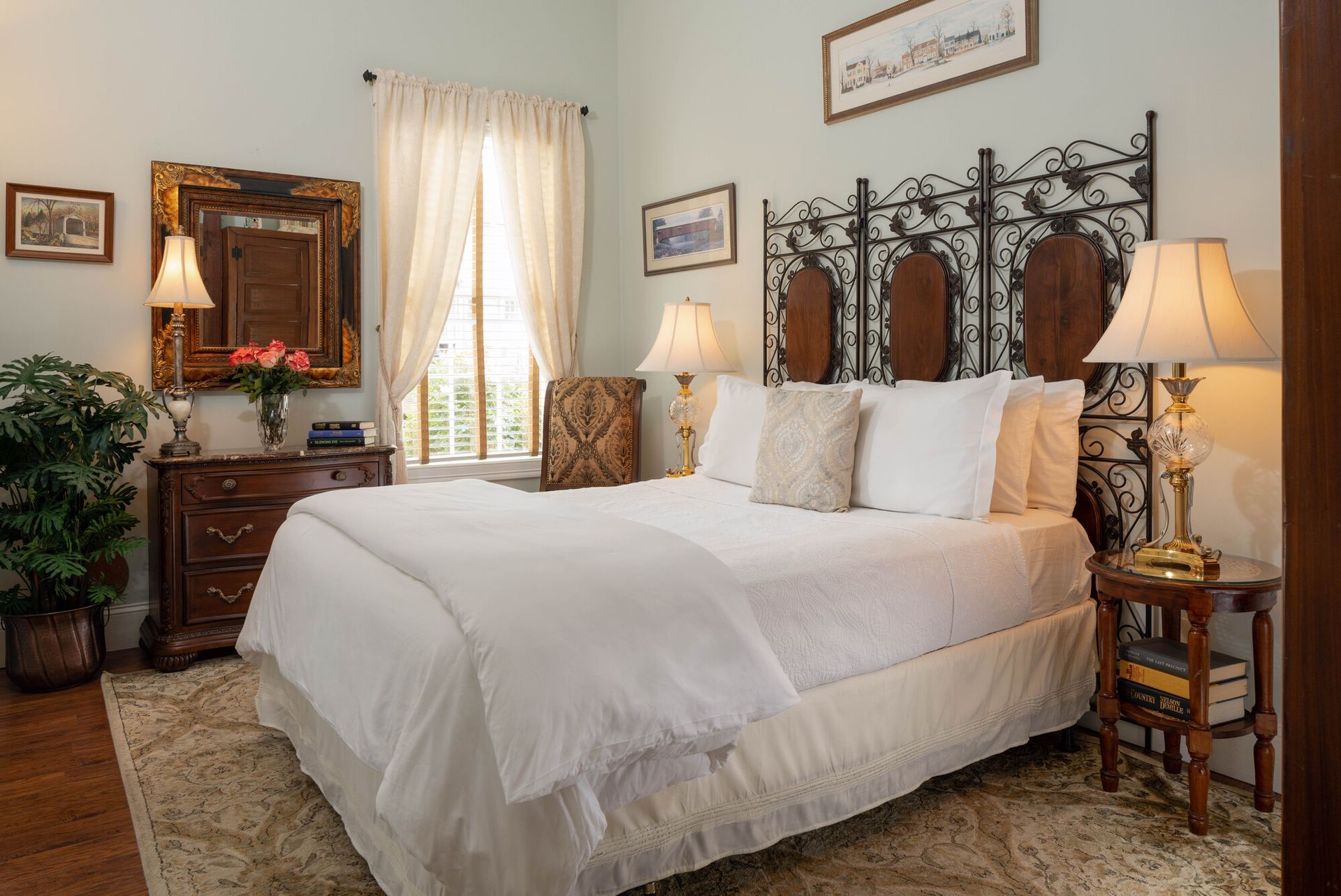 A bright, elegant bedroom featuring a queen bed with a wrought-iron headboard, white linens, and bedside lamps.