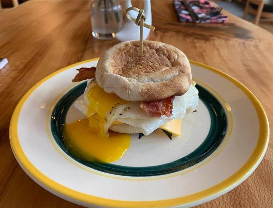 An egg and bacon breakfast sandwich on an English muffin, served on a white plate with yellow and green rims.