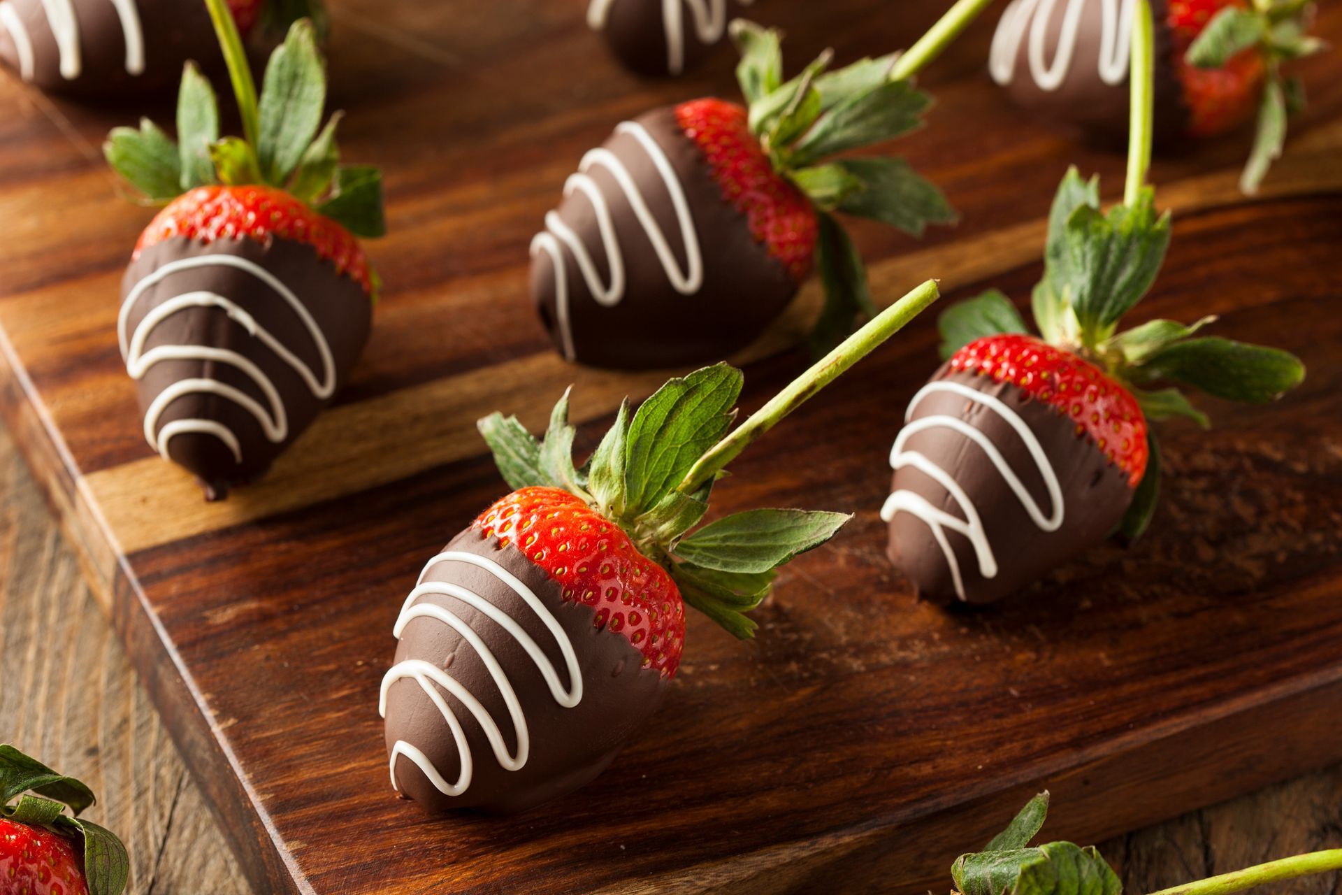 Fresh strawberries dipped in chocolate with white icing drizzles, arranged on a wooden cutting board.