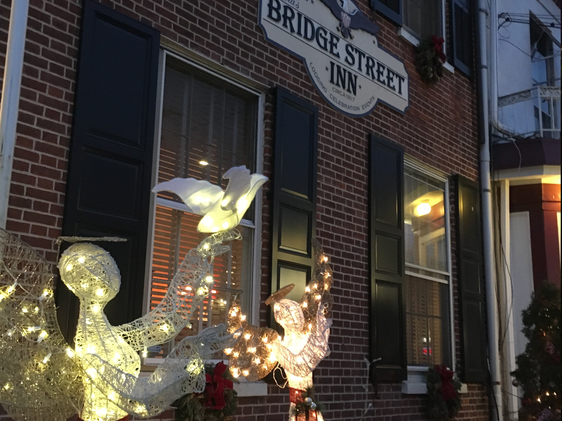 Illuminated angel decorations in front of the brick exterior of The Bridge Street Inn at dusk.
