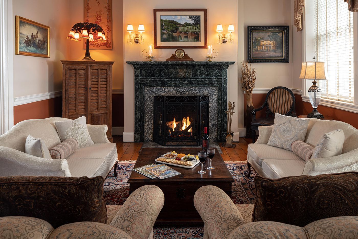 A formal living room with two beige sofas, a wooden coffee table, a fireplace with a marble mantel, and warm lighting.