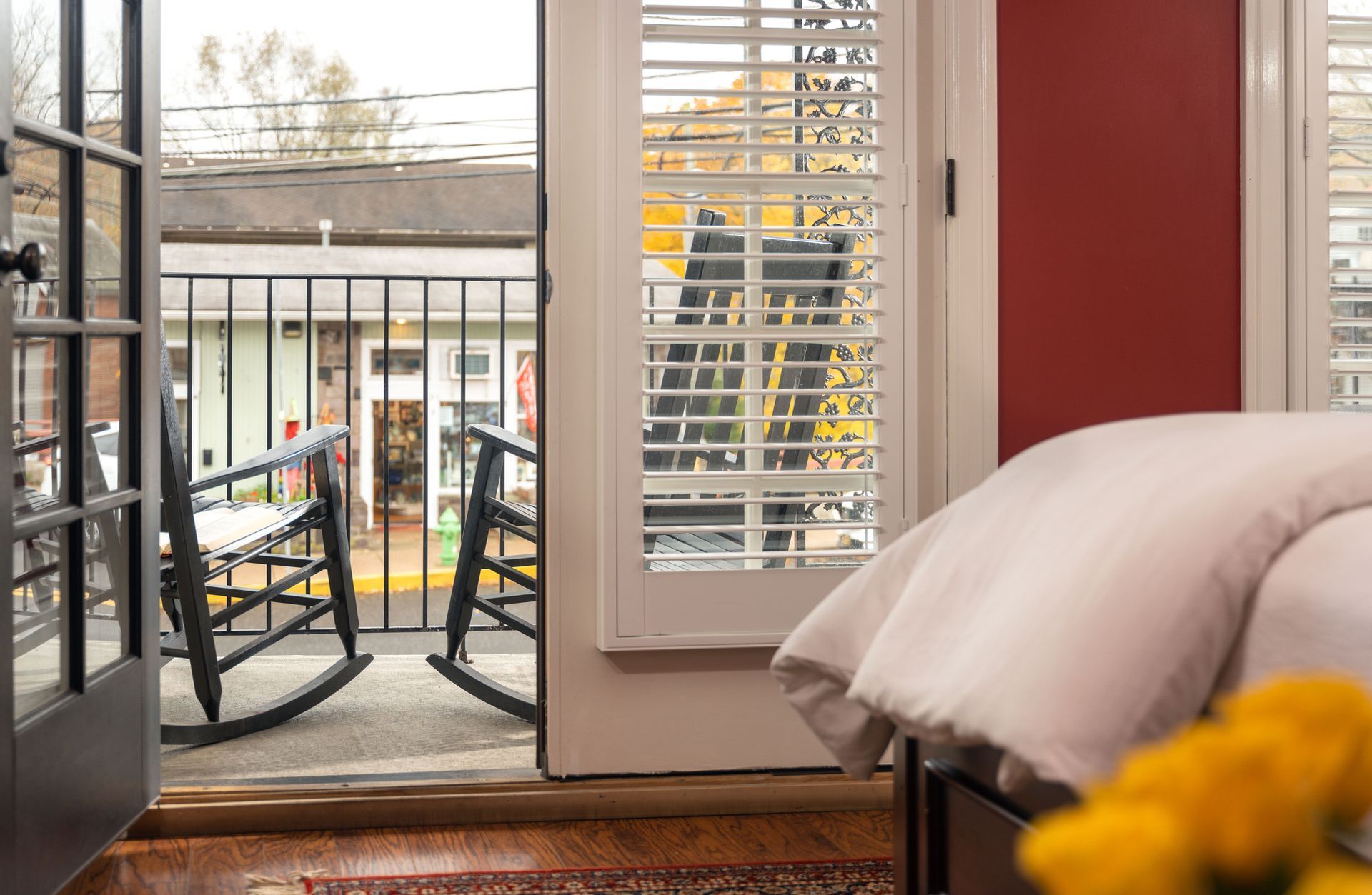 A balcony view from a bedroom features two dark wooden rocking chairs looking out toward a small town storefront.