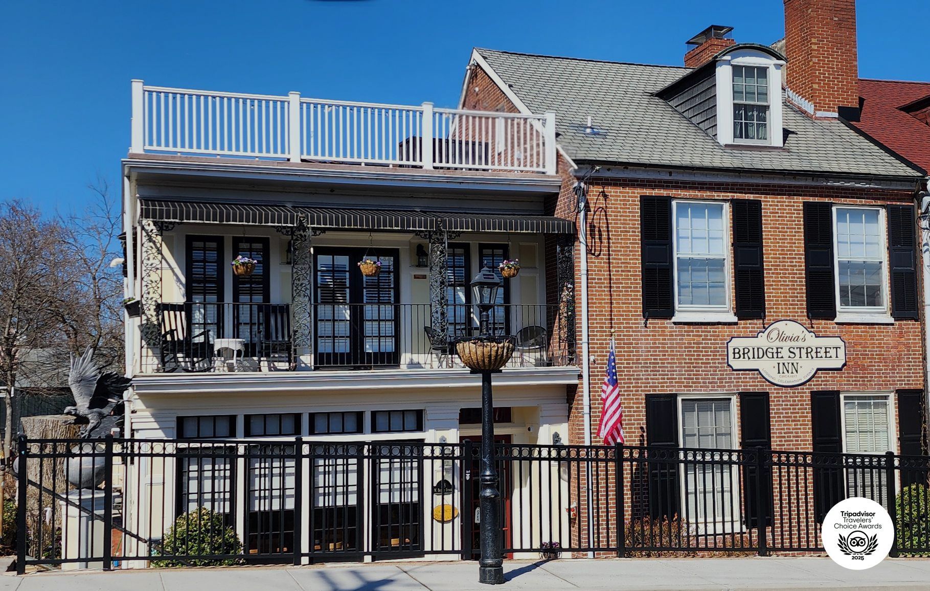 Two historic buildings stand side-by-side, one a white two-story structure with a balcony and the other a brick house.