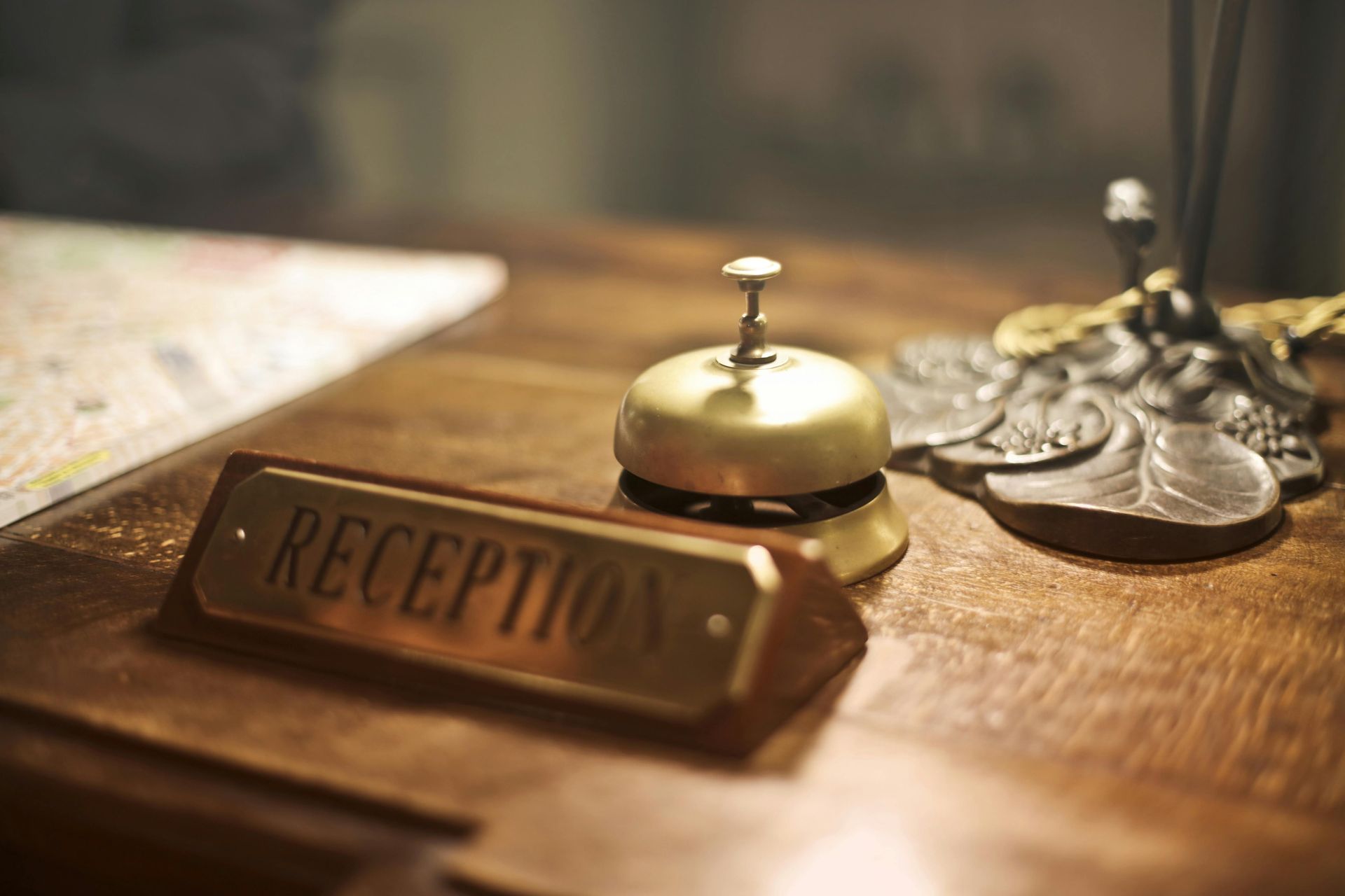 A brass hotel reception bell sits on a wooden desk next to a metal plaque labeled 