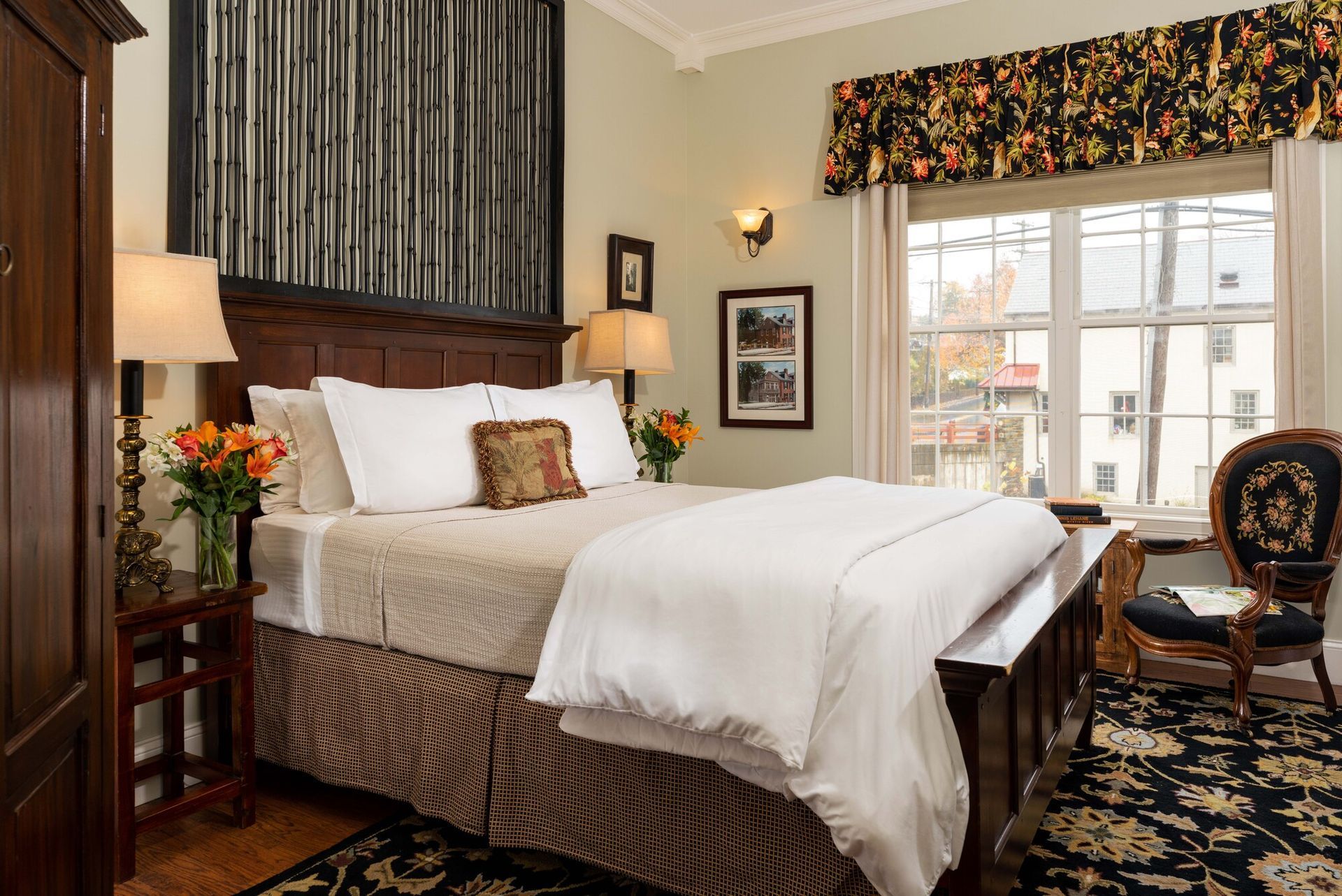 A cozy bedroom featuring a queen bed with white linens, a dark wooden headboard, and a patterned rug near a window.