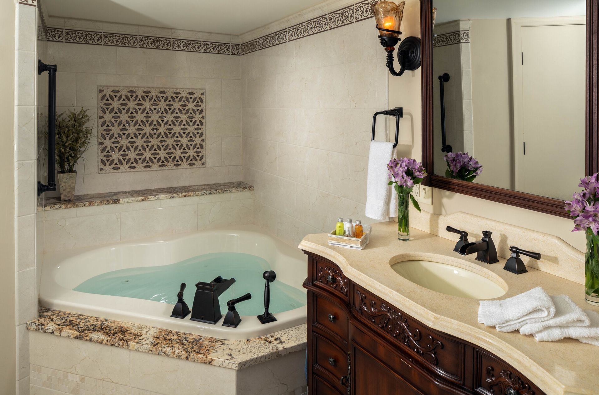 A bathroom featuring a corner soaking tub with dark fixtures and a wooden vanity with a cream countertop and mirror.