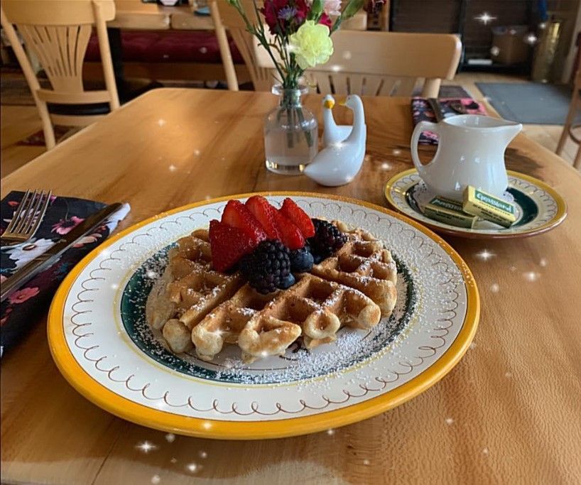 A golden waffle topped with strawberries and blackberries, served on a yellow-rimmed plate on a wooden café table.