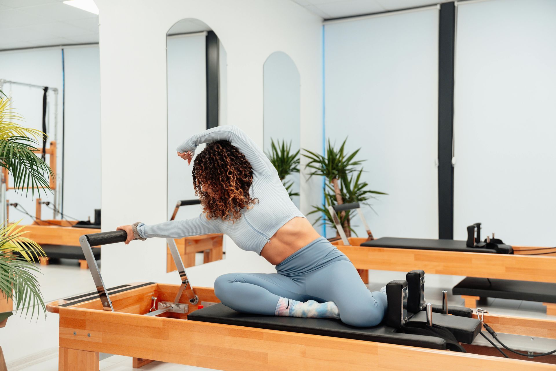 Woman in workout gear doing pilates stretch on wooden reformer in a studio.