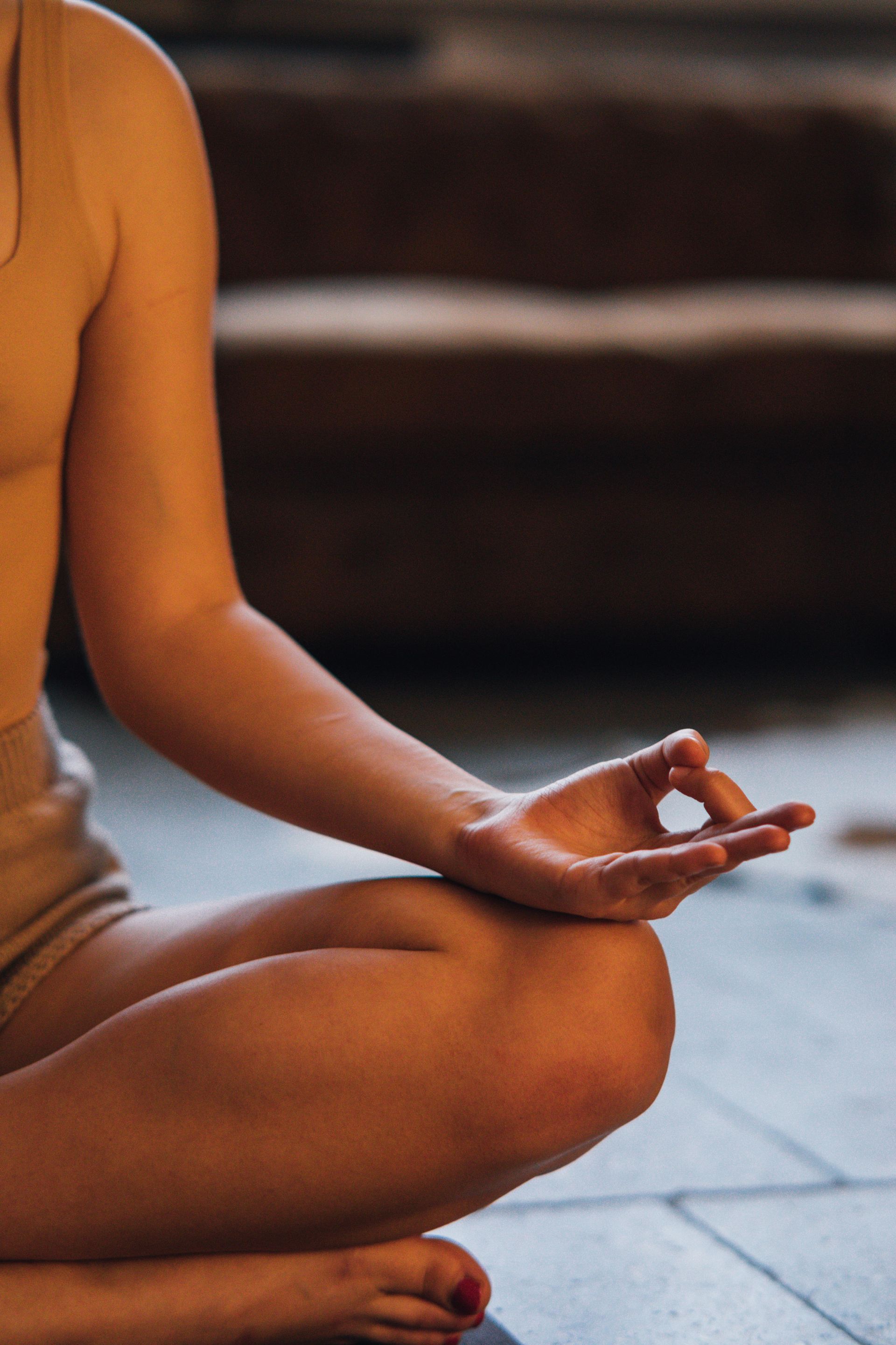Person meditating, hand in Gyan mudra position, legs crossed, light skin, blurred background.