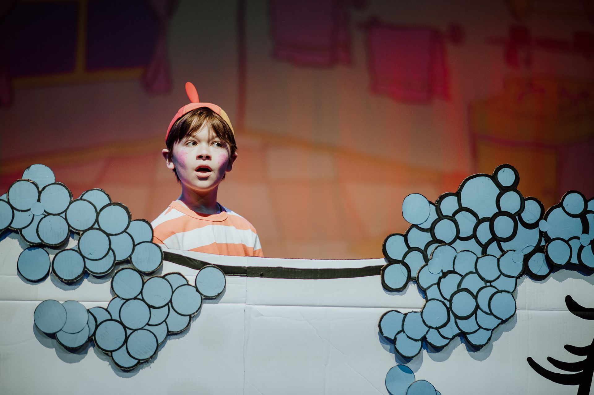 Boy in costume, surprised, looking over tub filled with blue bubbles. Stage set: bathroom.