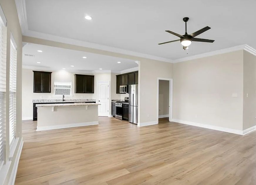 There is a ceiling fan in the living room and a kitchen in the background.