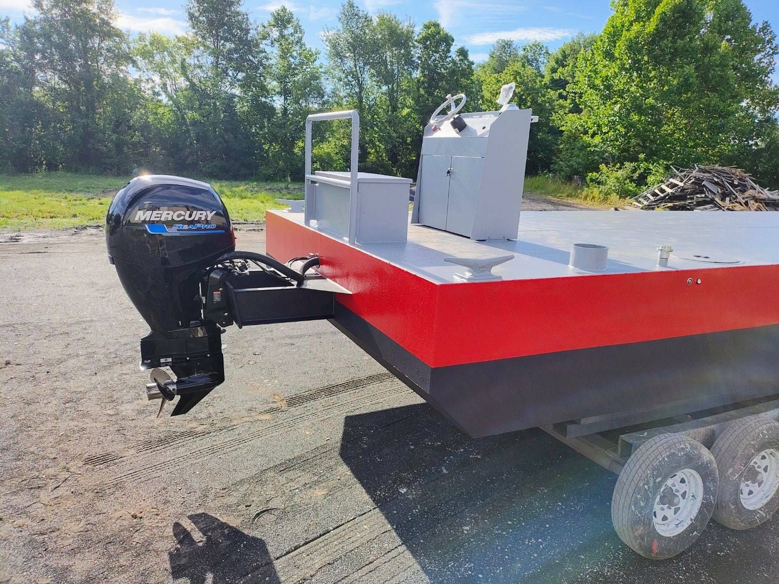 Red and black pontoon boat with a motor, on a trailer, outside.