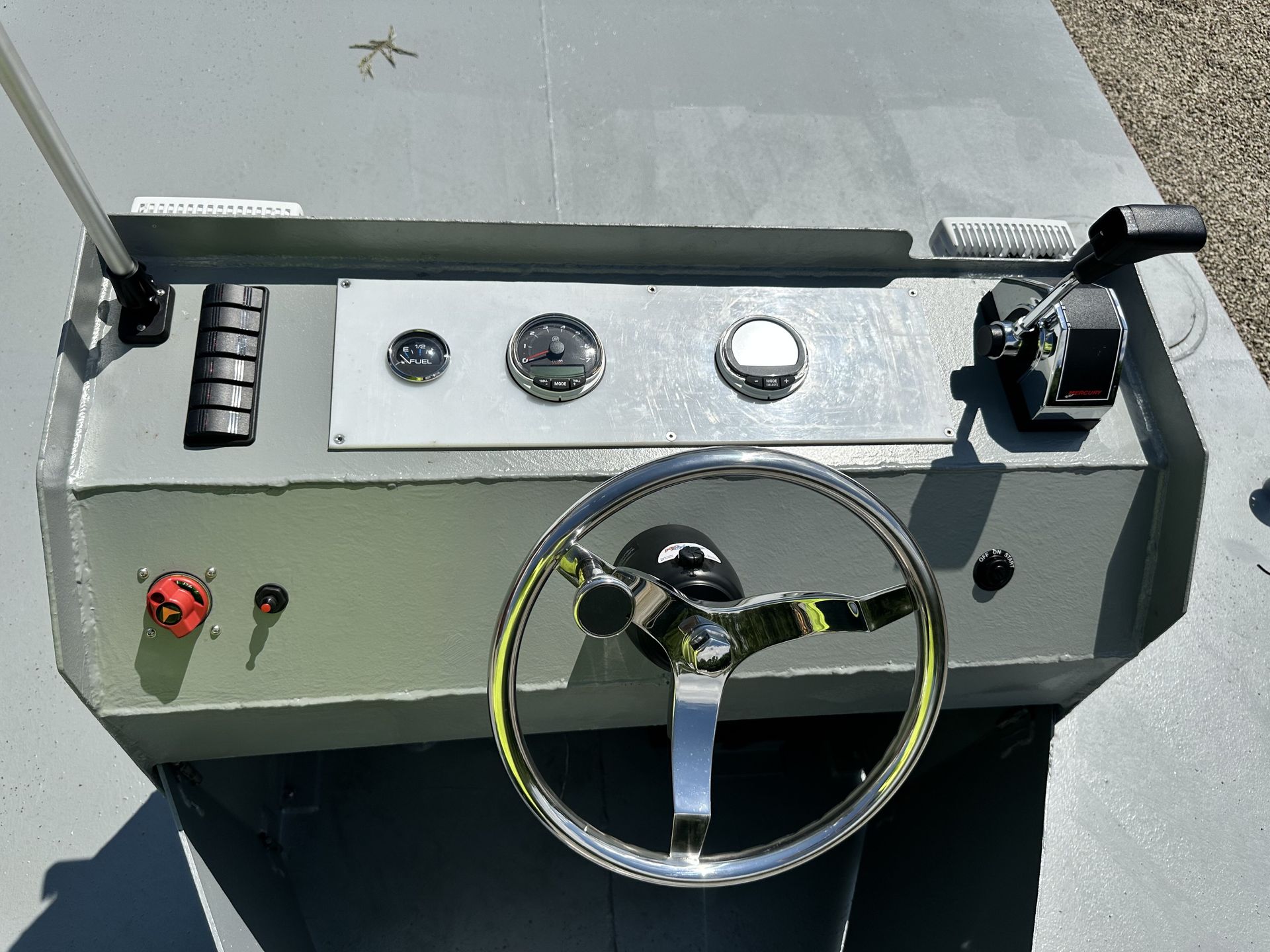 Boat dashboard with steering wheel, gauges, and controls. Gray with chrome accents.