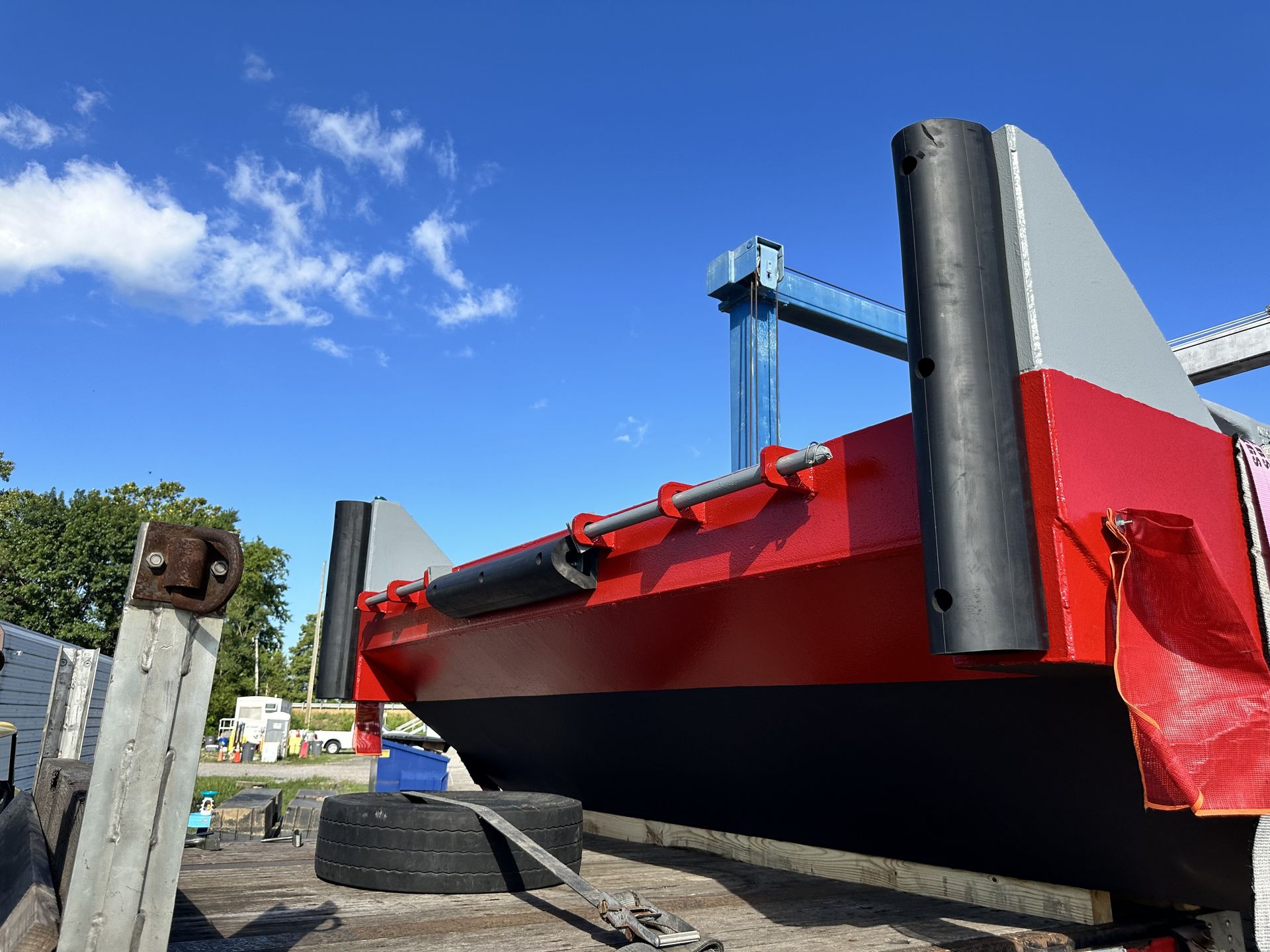 Red and black barge with large black fenders, parked outside against a blue sky.