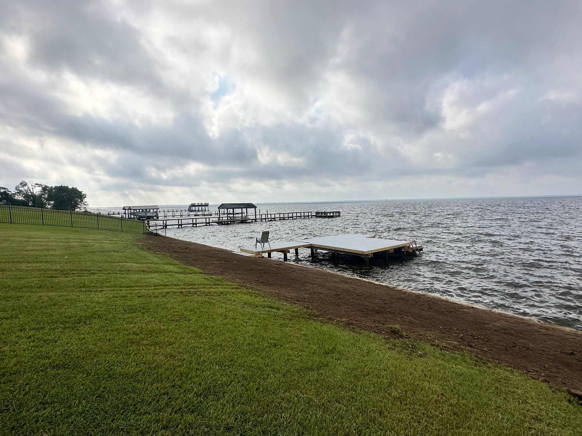 A cloudy day over a lake with docks. Green grass in the foreground and a retaining wall.