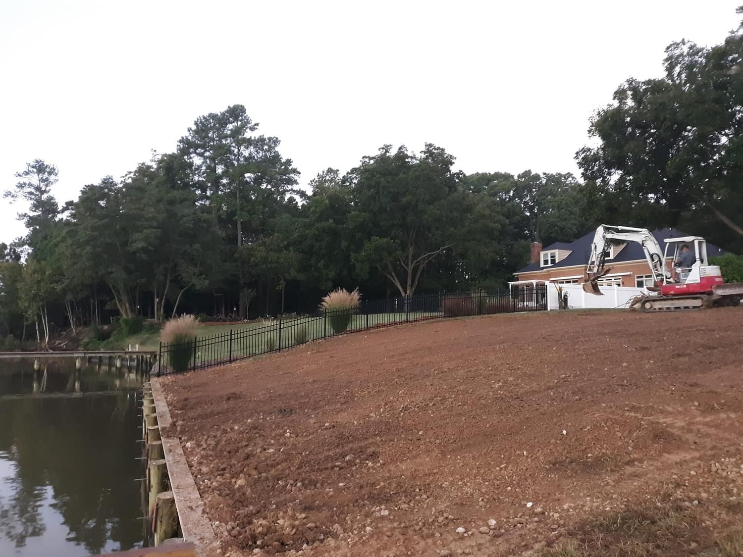A brown, dirt hillside next to a lake with construction equipment and trees.