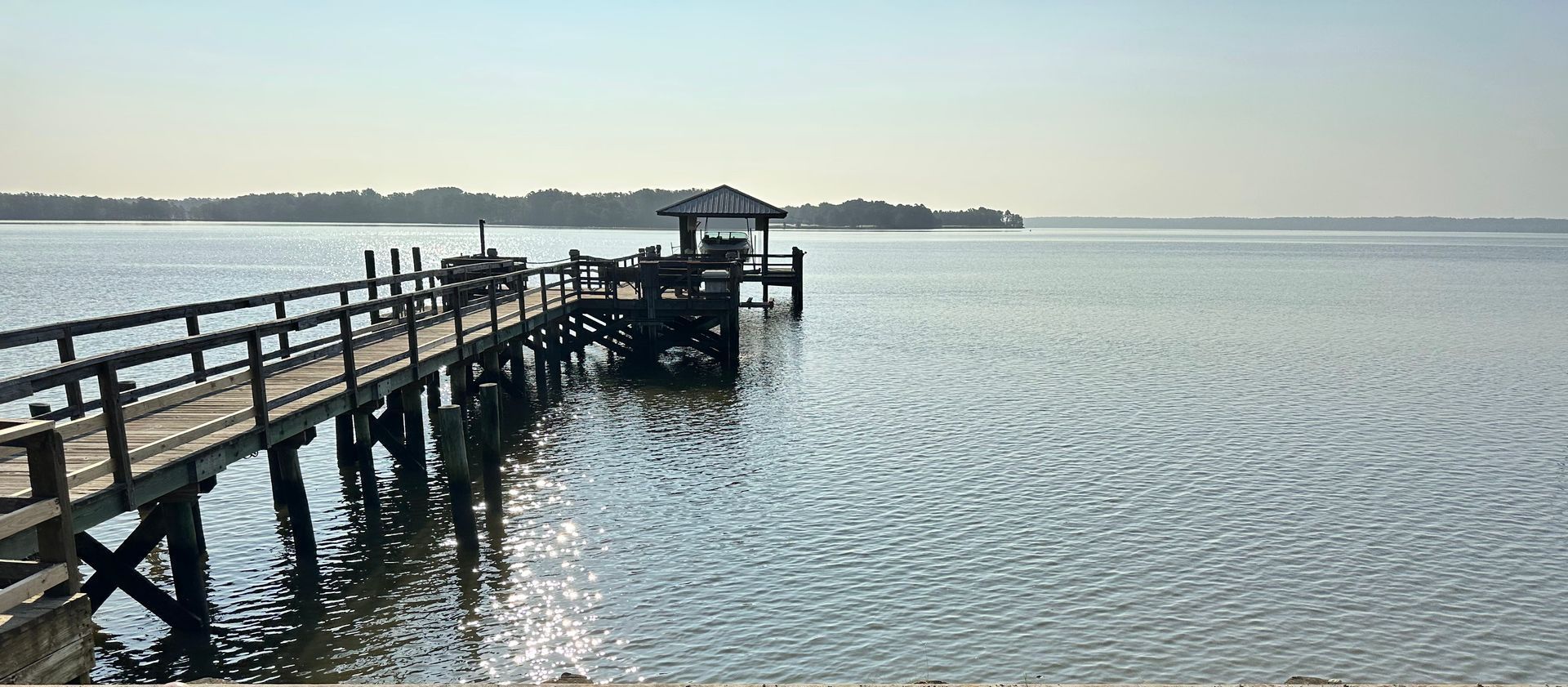 Wooden pier extending over calm water; gazebo at the end. Trees line the horizon.