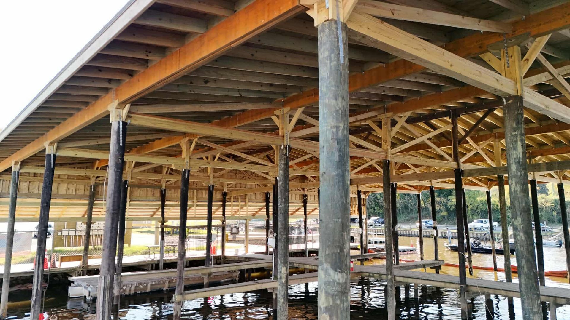Wooden boat dock with roof, supported by dark posts, over water.