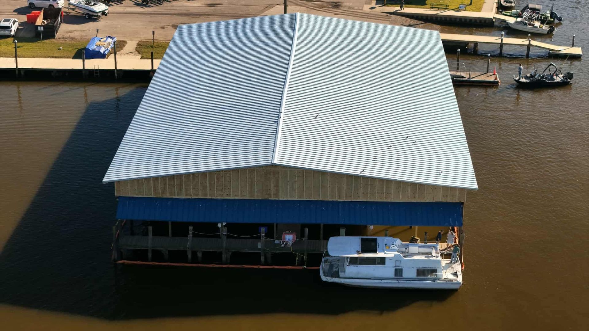 Boathouse with silver roof over a white boat in water. Blue trim, docks, and other boats nearby.