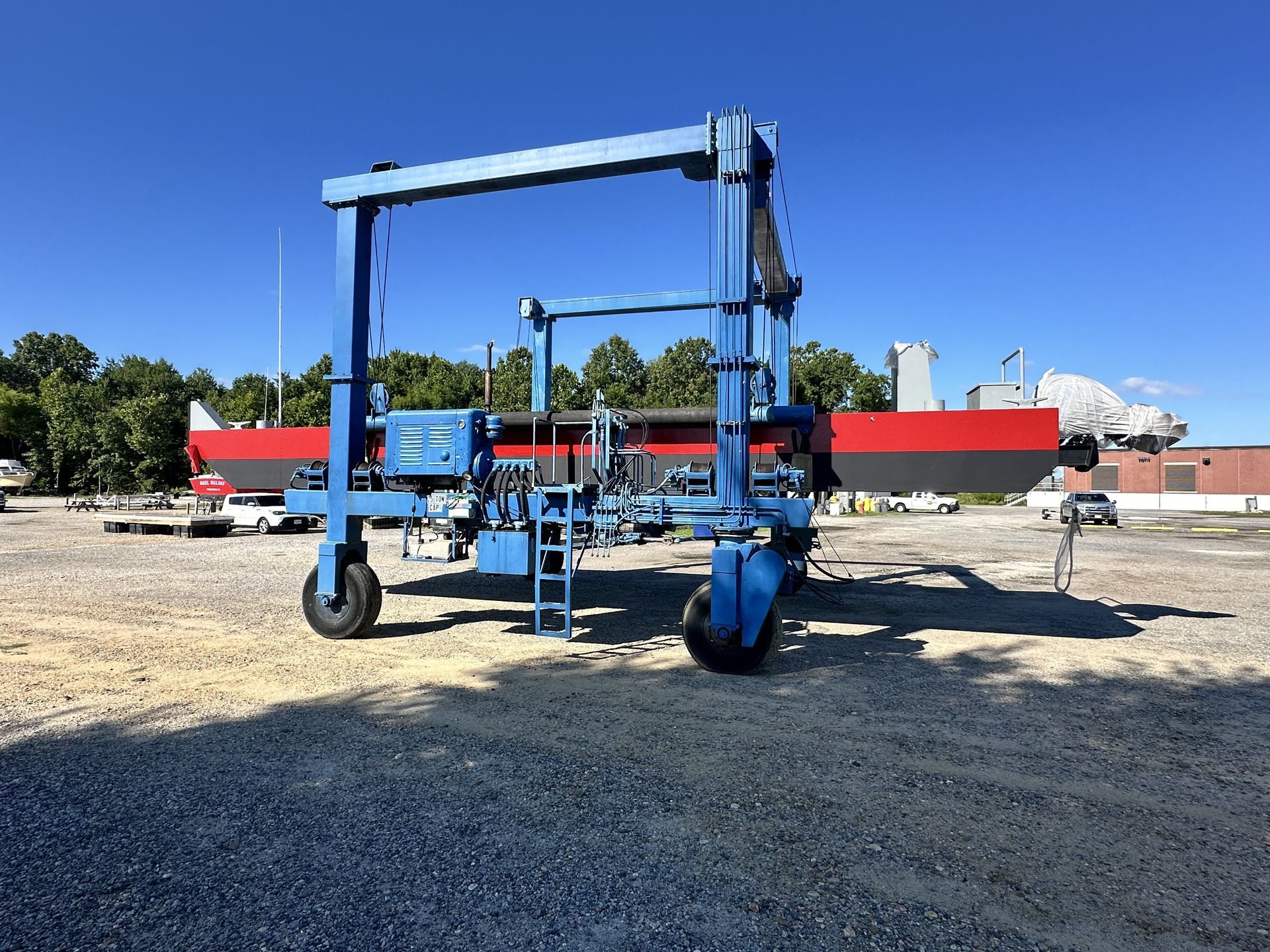 Blue boat lift in a gravel yard, with a partially visible red and black boat in the background.