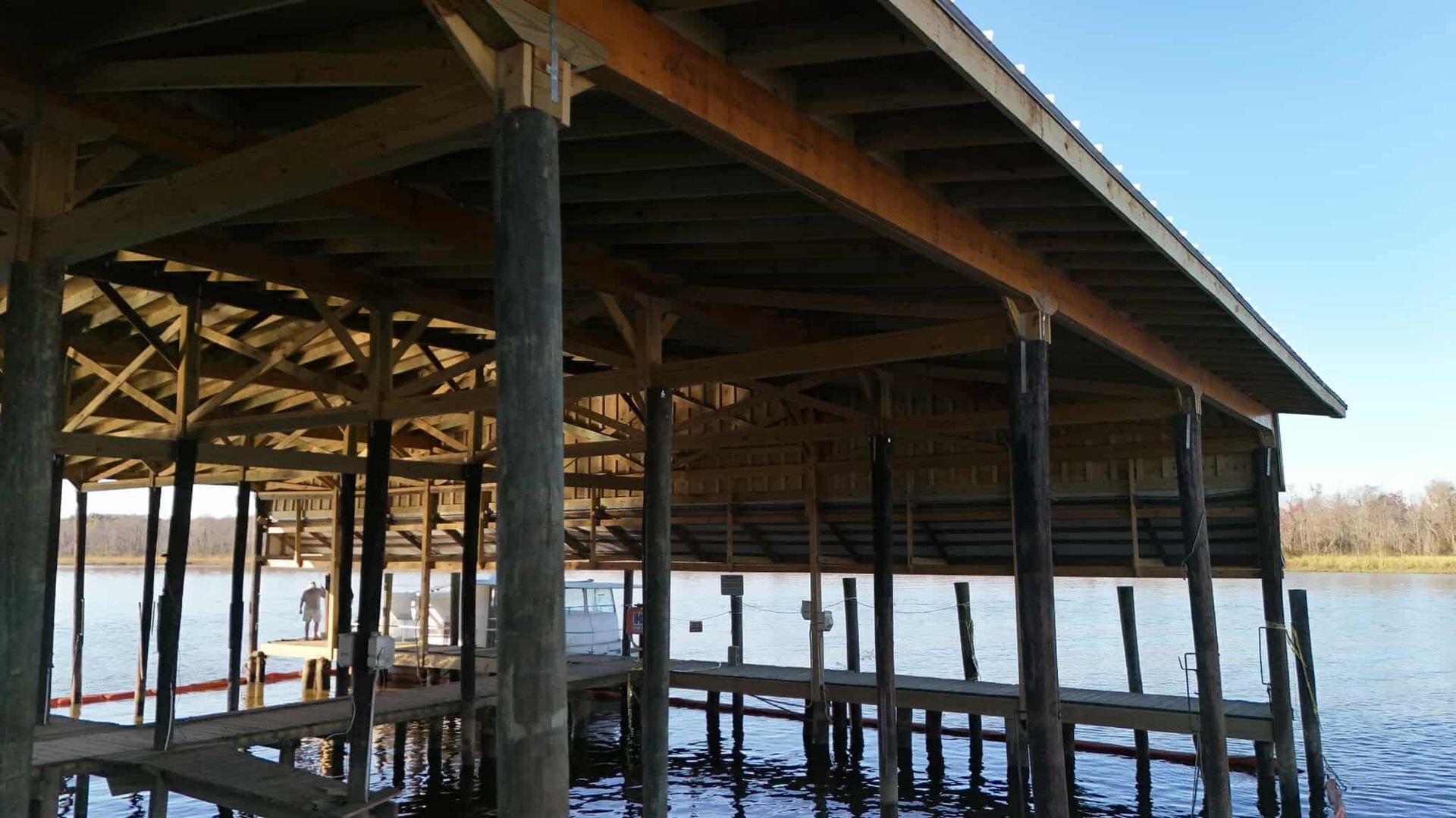 Wooden boathouse over water with supports, roof, and view of the lake.