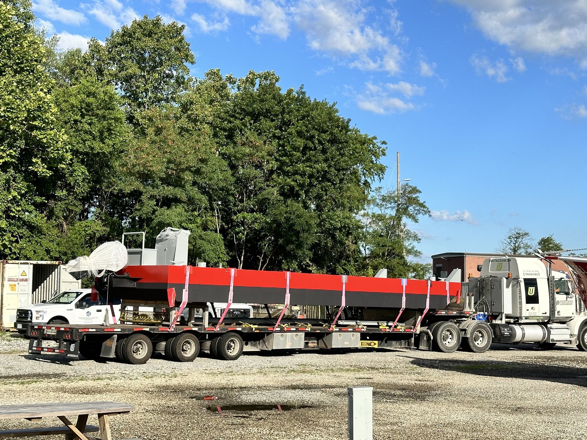 Truck transporting a long, red and black object on a flatbed trailer, in an outdoor setting.