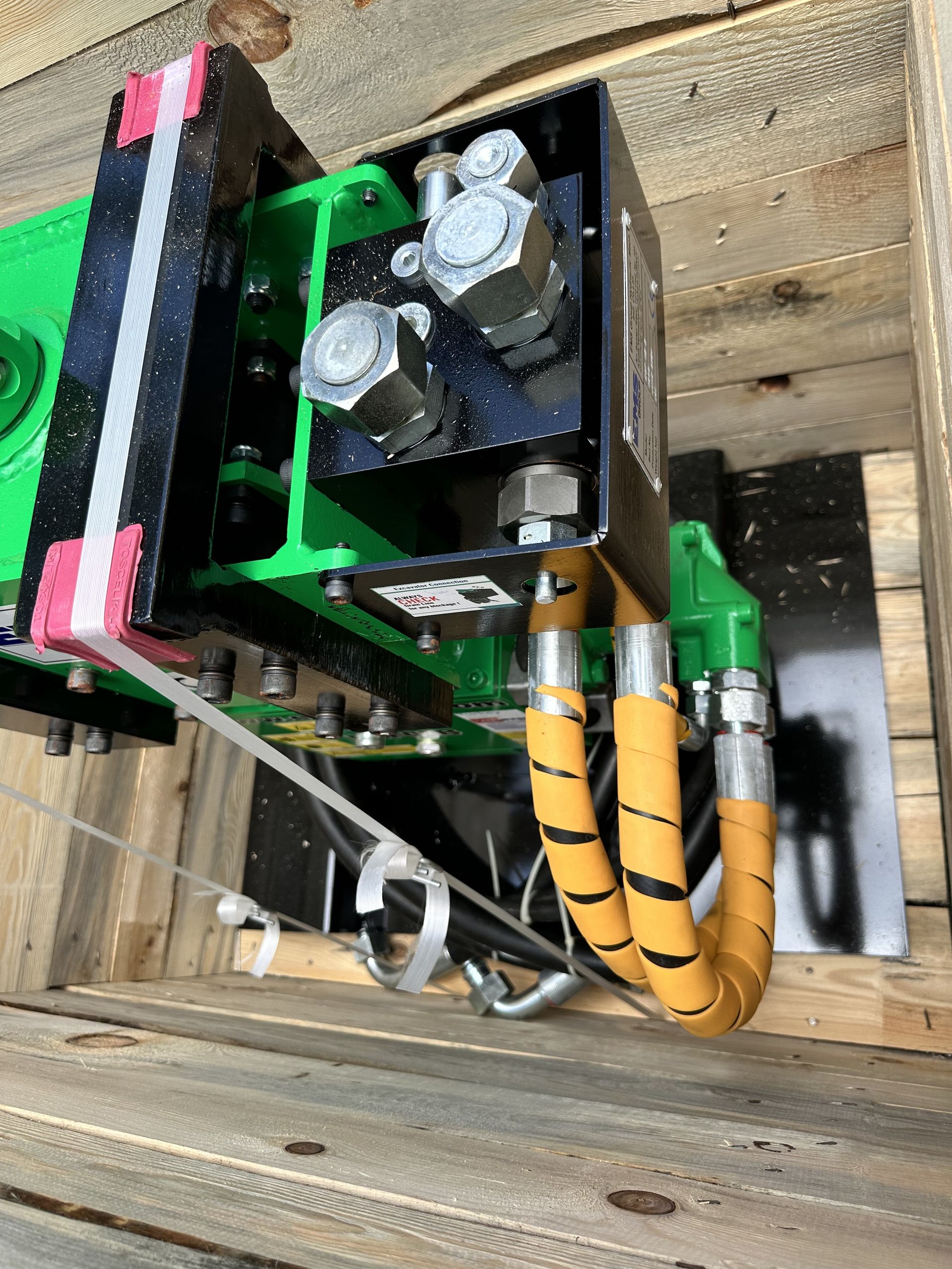 Green and black industrial machine with hydraulic hoses, mounted in a wooden crate.