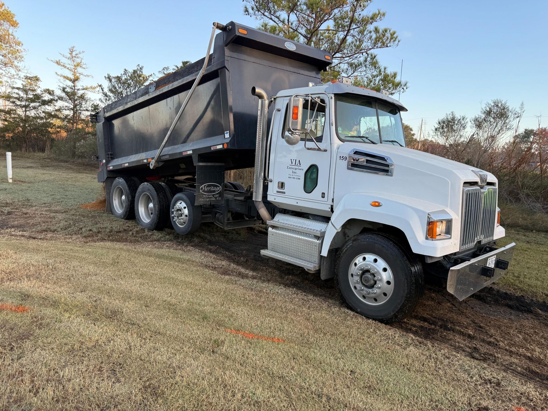 White dump truck parked on dirt in a field, with trees in the background.