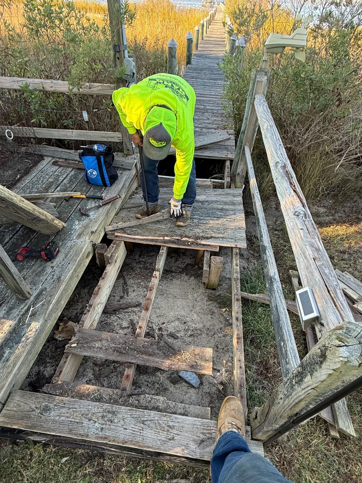 Man in neon jacket repairing damaged wooden stairs outdoors.