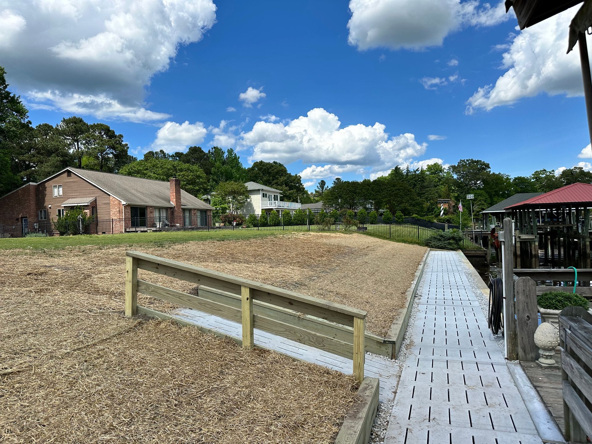 Wooden dock leads to a gravel area near a brick building under a blue sky.
