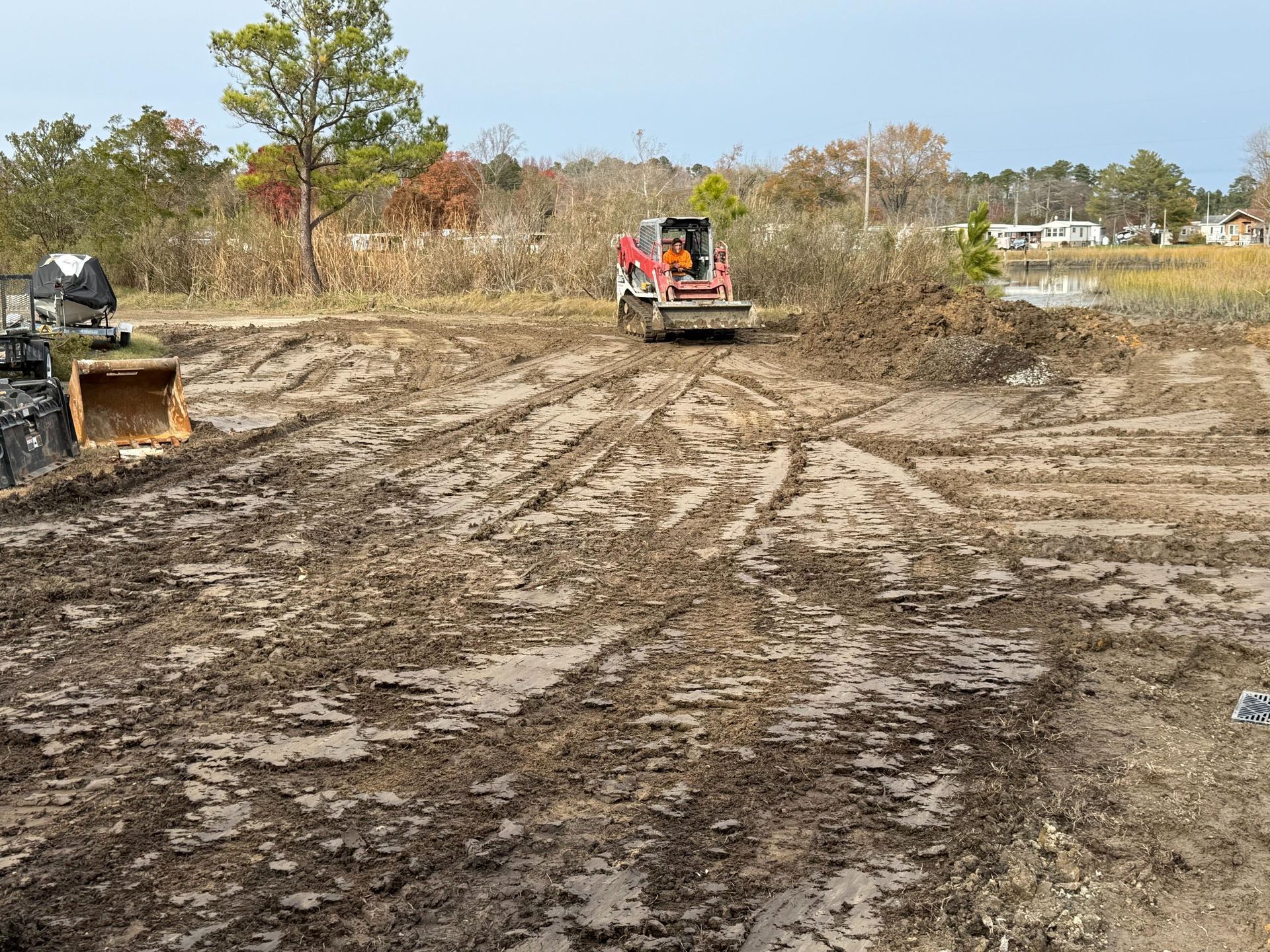 Muddy construction site with a red skid steer clearing brush.