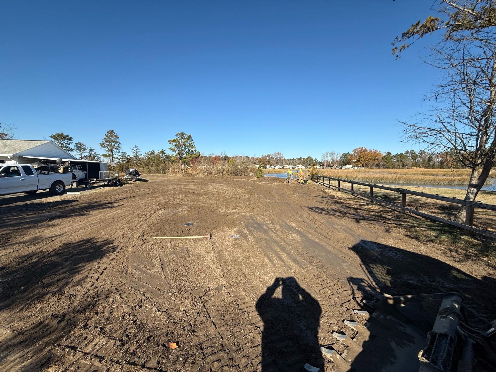 Dirt lot with truck, tent, fence, water, and clear blue sky.