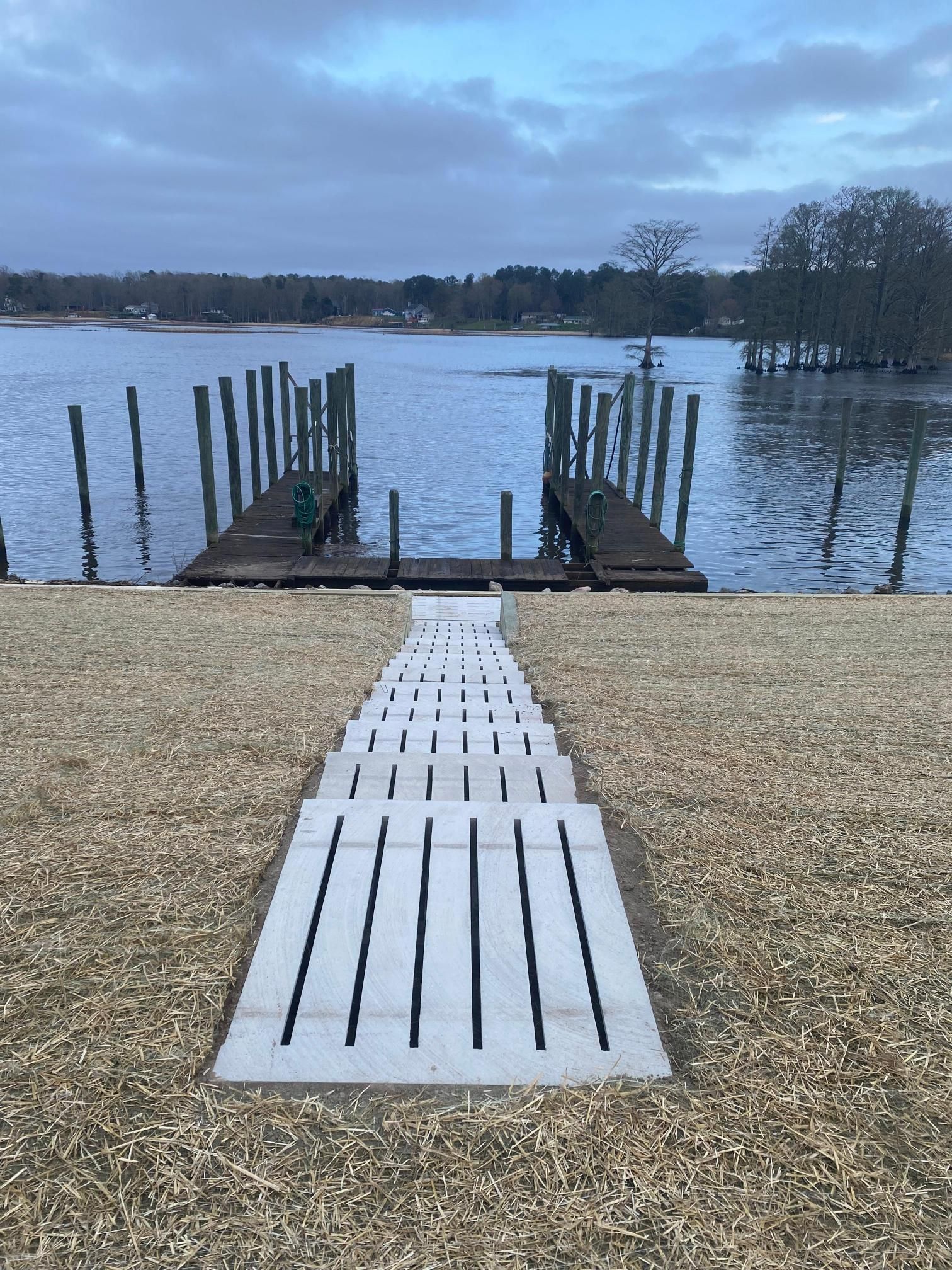 Stone steps lead to a wooden dock on a lake under a cloudy sky.