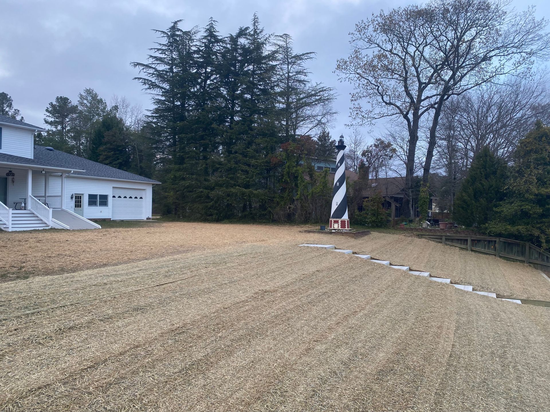 A black and white lighthouse sits on a gravel lawn. A white house is to the left.
