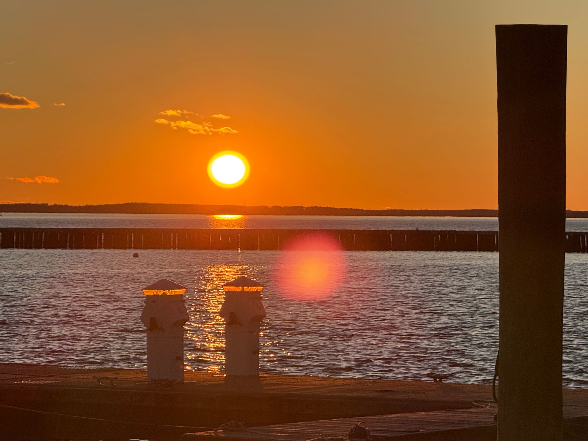 Sunset over water with two white lights and a dark pillar in the foreground.