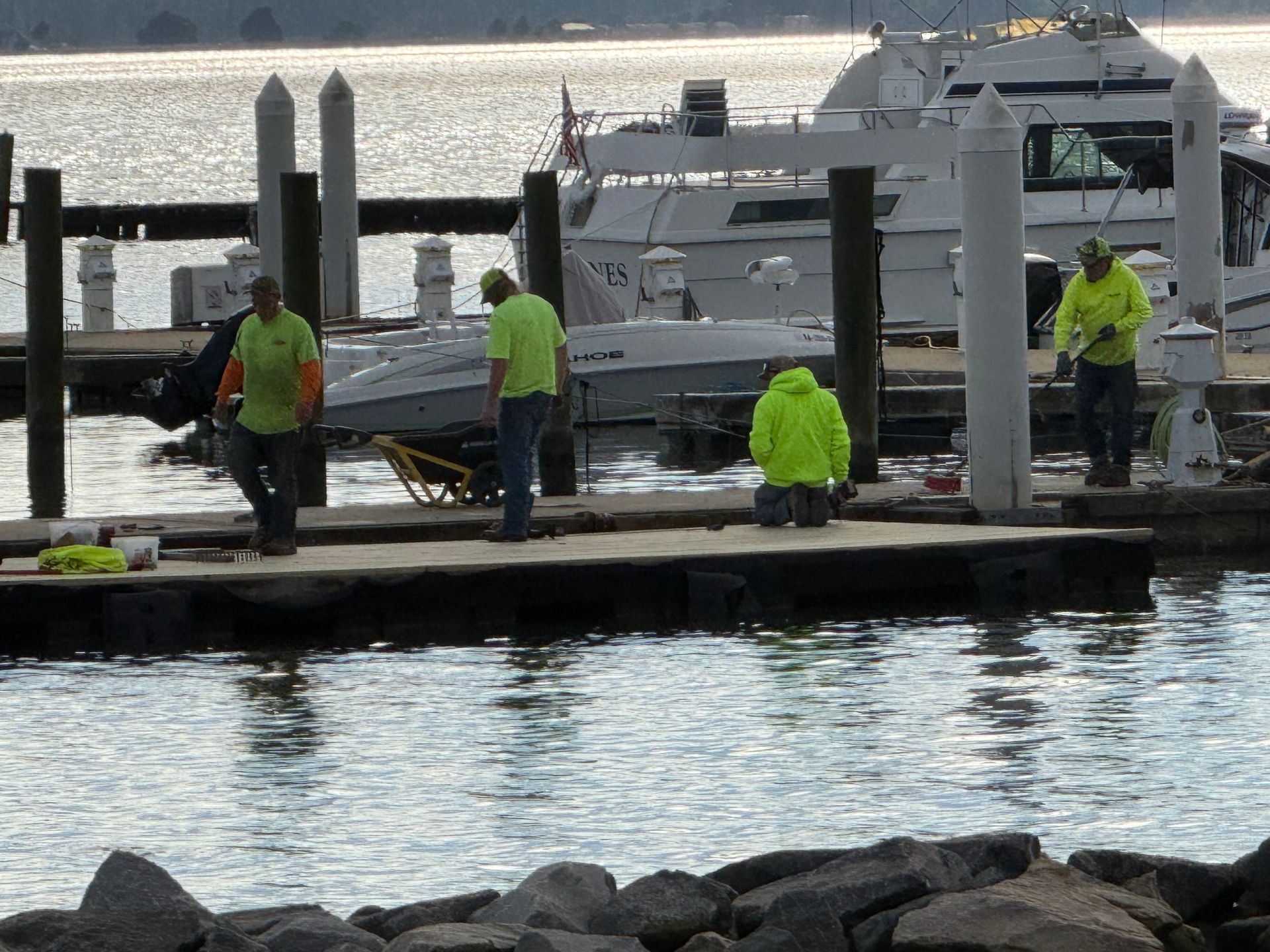 Workers in neon vests repair a dock near boats on a lake.