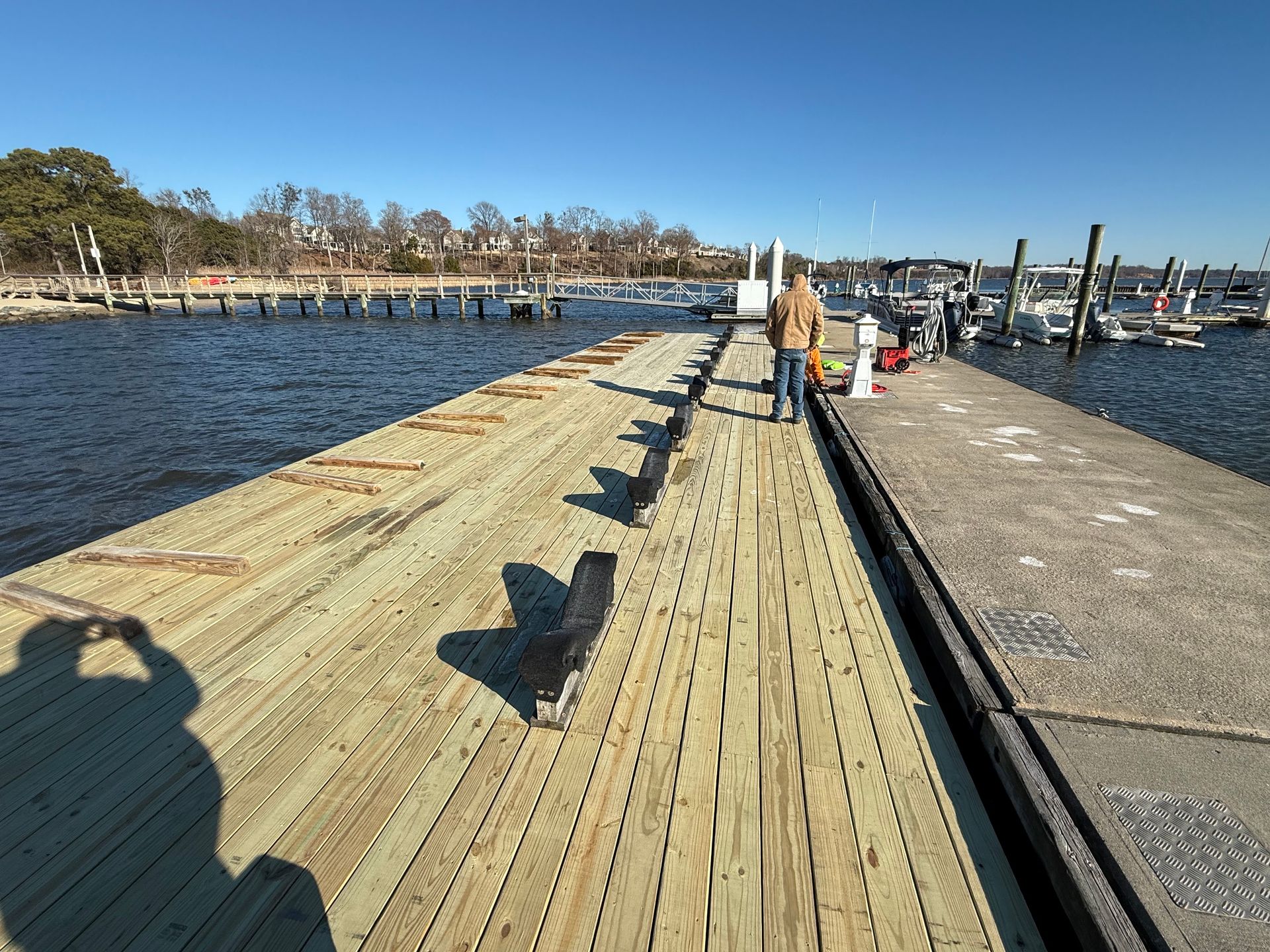 Man walking on a newly constructed wooden pier over water; sunny day with shoreline in the background.