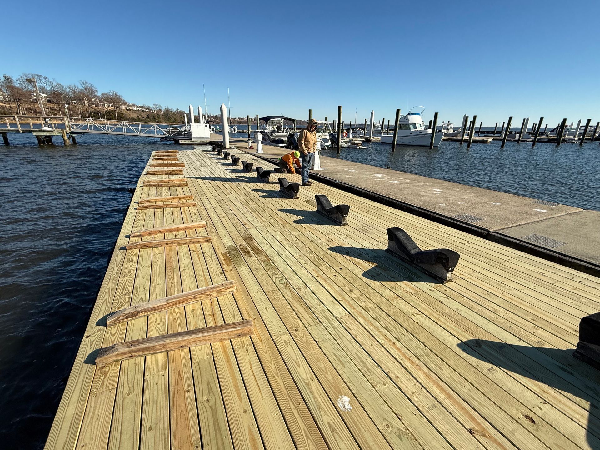 A partially constructed wooden dock with workers on it, in a harbor on a sunny day.