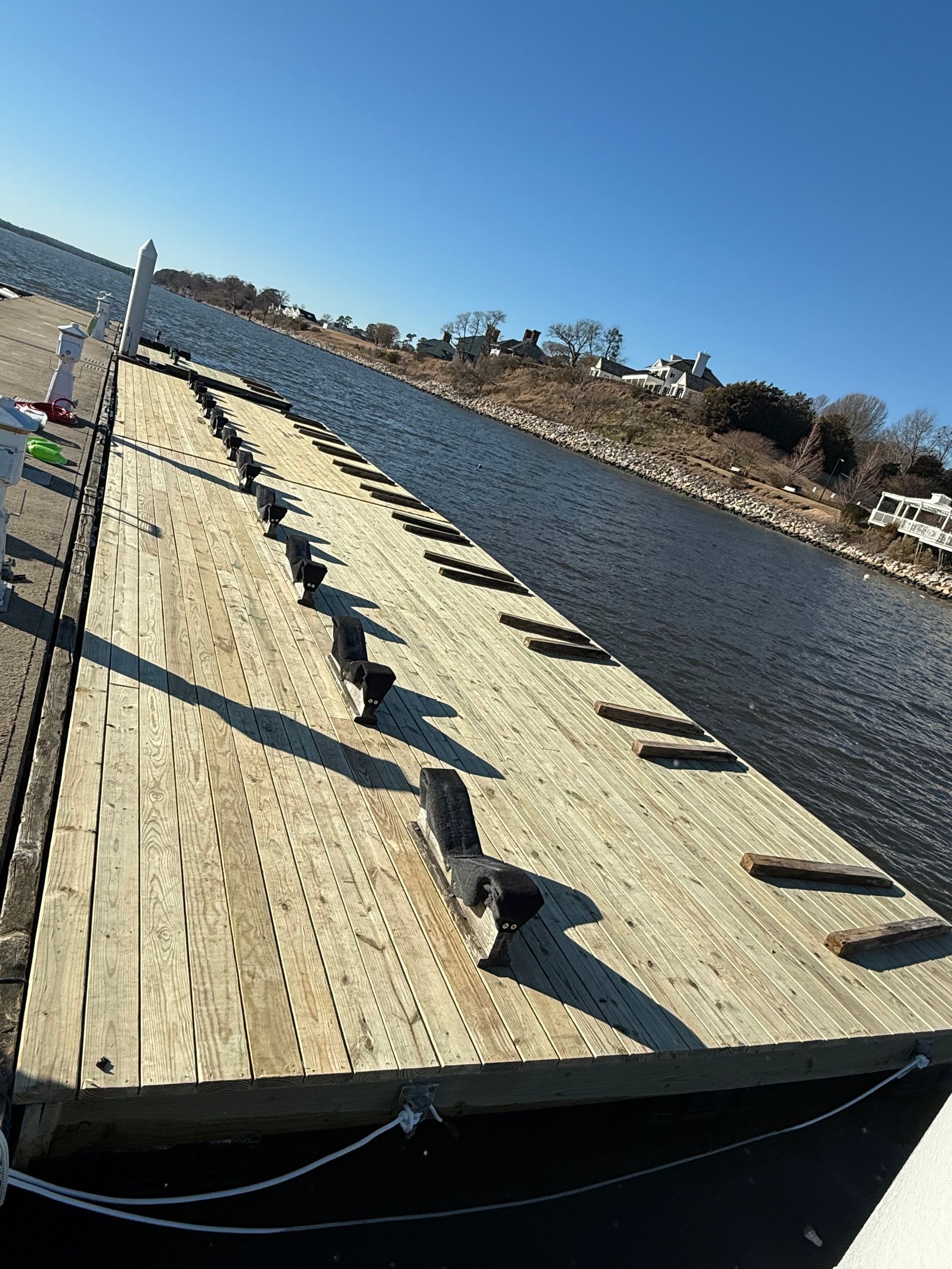 Wooden pier extending into water with cleats, against a sunny blue sky.